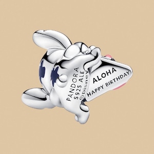 Puede incluir: Un charm de plata con un dise&ntilde;o de personaje de dibujos animados. El charm tiene un cuerpo blanco con detalles azules y un detalle rosa. Presenta el texto "ALOHA HAPPY BIRTHAY" en una pancarta y "PANDORA S925 ALE Disney" en el cuerpo.