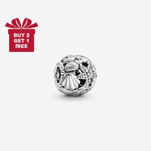 Könnte beinhalten: Ein silberner Charm mit einem detaillierten Design aus Muscheln und einem Seestern. Der Charm ist kugelförmig und hat eine polierte Oberfläche. Das Bild enthält auch eine rote Geschenkbox mit dem Text "BUY 2 GET 1 FREE".