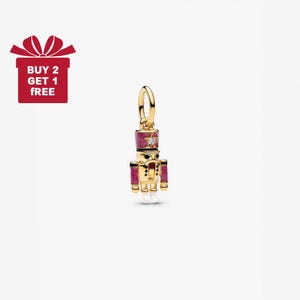 May include: A gold-colored charm in the shape of a nutcracker soldier. The charm features a red and gold uniform, a star-shaped gem, and a red hat. The charm is designed for a bracelet or necklace.