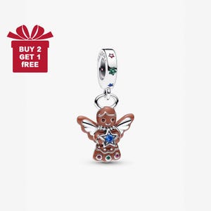 Puede incluir: Un charm de ángel de pan de jengibre marrón con alas plateadas, una estrella azul y gemas de colores. El charm está suspendido de un anillo plateado y una banda plateada con detalles de estrellas y gemas. La imagen incluye una caja de regalo roja con el texto "BUY 2 GET 1 FREE".