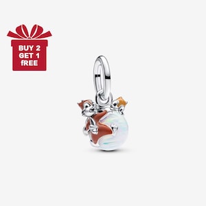 Puede incluir: Un charm de plata con dos ardillas de dibujos animados en esmalte marrón y naranja, abrazando un orbe iridiscente blanco. El charm tiene un lazo plateado. La imagen también incluye una caja de regalo roja con el texto "BUY 2 GET 1 FREE".