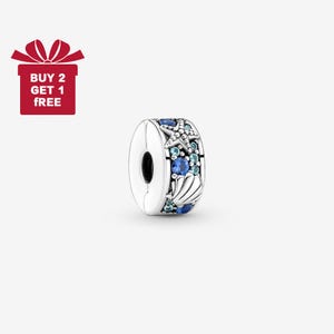 Puede incluir: Un charm de plata con un diseño de vida marina. El charm presenta una estrella de mar, conchas marinas y piedras preciosas azules. El charm tiene un cierre que se abre y se cierra. La imagen también incluye una caja de regalo roja con el texto "COMPRA 2 Y LLÉVATE 1 GRATIS".
