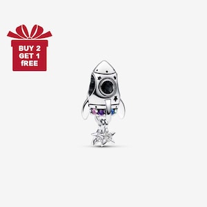 May include: A silver rocket charm with black portholes, star accents, and colourful gemstones. The charm has a star-shaped base and is designed to be a pendant or charm. The image also includes a red gift box with the text "BUY 2 GET 1 FREE."
