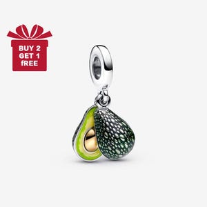 May include: A silver charm featuring a detailed avocado design. One half of the avocado is open, revealing a gold-colored pit and a bright green interior. The other half is a dark green with a textured pattern. The charm has a silver loop at the top. The image also includes a red gift box with the text "BUY 2 GET 1 FREE".