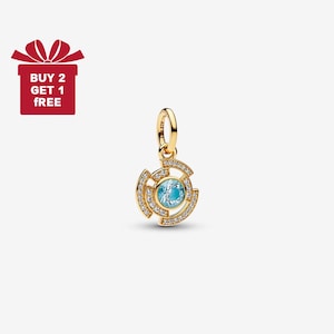 May include: A gold-colored pendant with a circular design, featuring a light blue center stone and surrounding clear crystals. The pendant has a loop for a chain. A red gift box with the text "BUY 2 GET 1 FREE" is in the upper left corner.