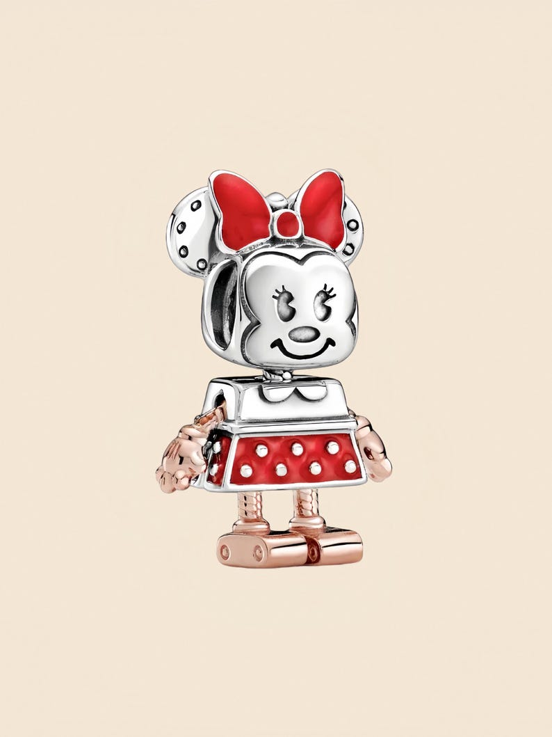 Pode incluir: Um charm da Minnie Mouse com cabe&ccedil;a prateada, la&ccedil;o vermelho e vestido vermelho com bolinhas brancas. O charm tem bra&ccedil;os e pernas em ouro rosa. Um item de colecionador. O charm foi projetado para ser adicionado a uma pulseira ou colar.