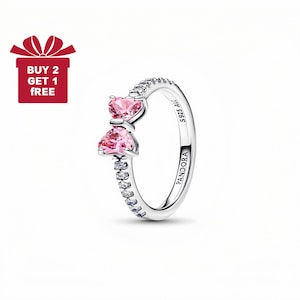 Puede incluir: Un anillo plateado con dos piedras rosas en forma de corazón y una fila de pequeñas piedras transparentes. La banda del anillo está grabada con "S925 ALE" y "PANDORA". Una caja de regalo roja con el texto "BUY 2 GET 1 FREE" está en la esquina superior izquierda.