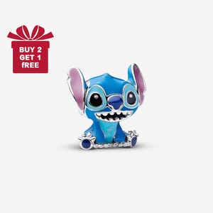 Könnte beinhalten: Ein blau-silberner Charm-Anhänger mit der Figur Stitch aus dem Disney-Film Lilo & Stitch. Der Charm hat große schwarze Augen, ein breites Grinsen und große Ohren mit rosa Innenseiten. Das Bild enthält auch eine rote Geschenkbox mit dem Text "BUY 2 GET 1 FREE".