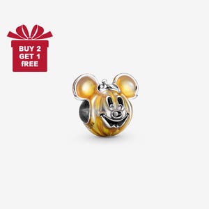 May include: A charm featuring a smiling Mickey Mouse face with a pumpkin-like design. The charm has a silver-colored face and ears, with a yellow and orange body. The text "BUY 2 GET 1 FREE" is in a red gift box.