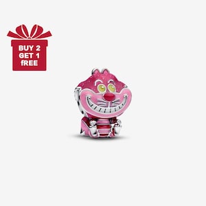 Pode incluir: Um berloque rosa e prateado com o Gato Cheshire de Alice no País das Maravilhas. O berloque tem um sorriso largo, olhos amarelos e um nariz vermelho. A imagem também inclui uma caixa de presente vermelha com o texto "BUY 2 GET 1 FREE".
