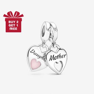 Puede incluir: Dos colgantes plateados en forma de corazón. Uno dice "Daughter" con un corazón rosa, el otro dice "Mother" con un recorte en forma de corazón. Los colgantes están conectados a un cierre plateado. Una caja de regalo roja con el texto "BUY 2 GET 1 FREE" está en la esquina superior izquierda.