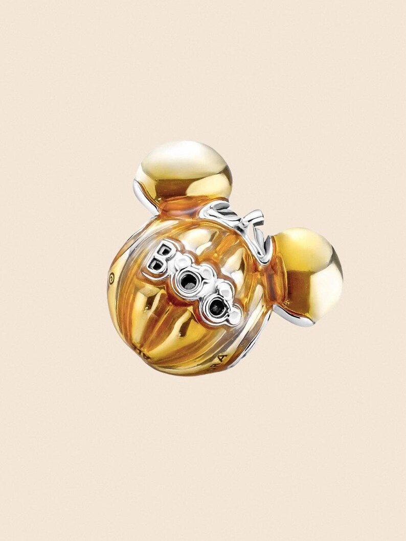 May include: A gold-colored charm with a Mickey Mouse head design. The charm features a ribbed body with the word "Boo" in silver lettering and two black accents. The charm has two gold-colored spheres on top.