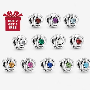 May include: A selection of silver charm beads, each with a coloured gemstone centre. Gemstones are in various colours, including red, purple, blue, green, and yellow. The image also includes a red gift box with the text "BUY 2 GET 1 FREE."