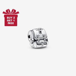 May include: A silver-colored charm in the shape of a school backpack. The charm has detailed features including buckles, a handle, and a small airplane design. The charm is on a white background.