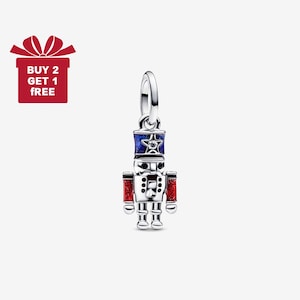 May include: A silver-coloured charm in the shape of a toy soldier, with a blue and red hat and red sleeves. The charm has a star on the hat and is hanging from a silver loop. A red gift box with the text "BUY 2 GET 1 FREE" is in the upper left corner.
