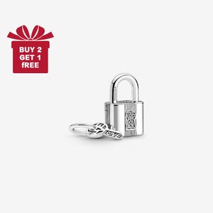 Puede incluir: Un charm de candado plateado con una llave. La llave tiene la palabra "LOVE" grabada. El candado tiene un diseño de ojo de cerradura con pequeñas piedras transparentes. La imagen también incluye una caja de regalo roja con el texto "BUY 2 GET 1 FREE".