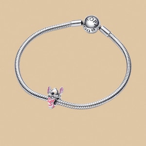Puede incluir: Una pulsera de plata con un charm de Stitch. El charm es una figura rosa y negra del personaje Stitch de la pel&iacute;cula de Disney Lilo & Stitch. La pulsera tiene un dise&ntilde;o de cadena de serpiente y un cierre redondo.