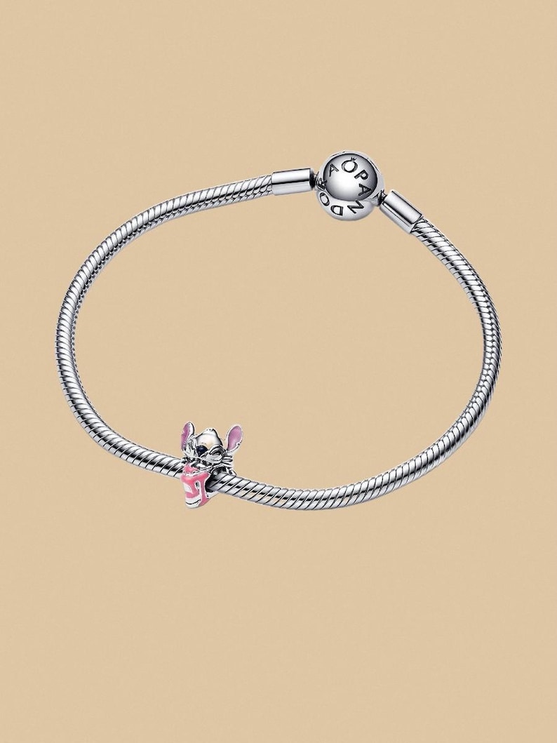 Puede incluir: Una pulsera de plata con un charm de Stitch. El charm es una figura rosa y negra del personaje Stitch de la pel&iacute;cula de Disney Lilo & Stitch. La pulsera tiene un dise&ntilde;o de cadena de serpiente y un cierre redondo.