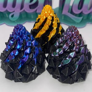 Op de afbeelding: Drie kleine, kegelvormige, 3D-geprinte objecten. De objecten zijn zwart met iriserende paarse, blauwe en gele accenten.