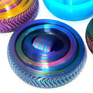 Op de afbeelding: Een close-up van een blauwe en iriserende draaitop met een golvende, getextureerde buitenrand. De draaitop is gemaakt van meerdere lagen materiaal, waardoor een draaiende, hypnotische effect ontstaat.