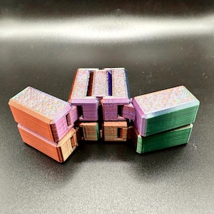 以下が含まれることがあります： モジュール設計のカラフルな幾何学的なフィジェットおもちゃ。おもちゃは、オレンジ、紫、緑の色合いのいくつかの長方形のブロックで構成されており、より大きな構造を形成するために接続されています。ブロックは、テクスチャ加工された虹色の外観をしています。