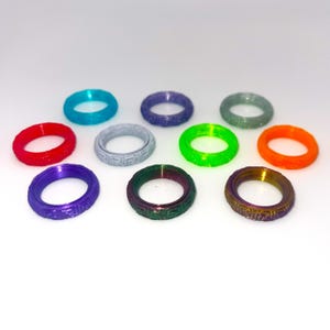 Op de afbeelding: Assortiment van tien kleurrijke ringen met een textuurontwerp. De ringen zijn gemaakt van plastic en zijn verkrijgbaar in verschillende kleuren, waaronder rood, oranje, geel, groen, blauw, paars en wit.