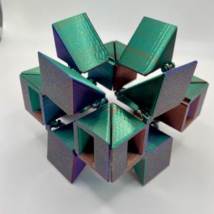 May include: A multi-faceted, iridescent, teal, purple, and brown geometric puzzle toy. The toy is made of plastic and has a unique design that allows it to be folded and unfolded in various ways.
