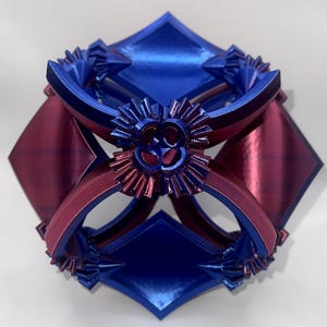 May include: A geometric sculpture with a complex design. The piece features a combination of blue and burgundy colors. The sculpture has a symmetrical arrangement of diamond shapes and curved elements, with intricate details.