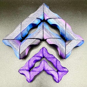 May include: Geometric, abstract sculptures in shades of blue, purple, and gray. The pieces are arranged in a symmetrical pattern, with a smaller purple sculpture at the bottom. The designs have textured surfaces and angular shapes.