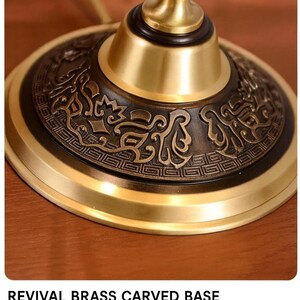 Pu&ograve; includere: Primo piano di una base di lampada in ottone con intricati dettagli scolpiti. La base ha una finitura bicolore, con una parte superiore dorata e una inferiore di tonalit&agrave; pi&ugrave; scura e antica. Il testo "REVIVAL BRASS CARVED BASE" &egrave; visibile.