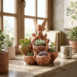 May include: A terracotta-colored planter shaped like a gnarled tree stump with multiple openings for plants. A small fairy figure with wings sits atop the central structure. The planter holds various green and purple succulents, including a trailing string of pearls.