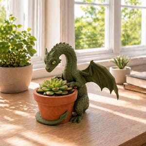 May include: A green dragon figurine cradles a terracotta pot with a succulent plant. The dragon has detailed scales, wings, and a curved neck. The plant pot is round and sits on a wooden surface, with a window and other plants in the background.