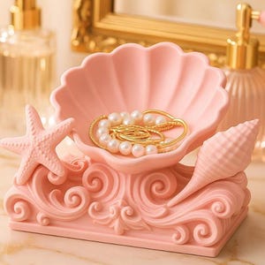 May include: A pink seashell-shaped jewelry holder with a starfish and conch shell accent. The holder contains gold jewelry with pearls. The base features a decorative wave design. A decorative item for storing jewelry.