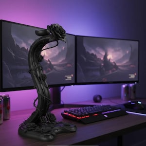 May include: A black rose-themed desk accessory with a curved stem and multiple rose buds. The accessory is placed in front of two computer monitors, a keyboard, and a mouse. The background has purple and blue lighting.