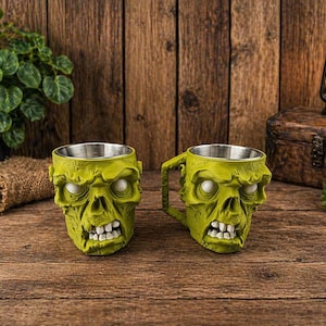 May include: Two zombie-themed mugs with stainless steel interiors. The mugs are lime green with white eyes and teeth, and are set on a wooden surface. One mug has a handle.