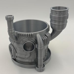 May include: A gray, 3D-printed steampunk-style container with a cylindrical body, pipes, and rivets. It features a small chimney and a larger, flared top, suggesting a unique design for holding items or as a decorative piece.