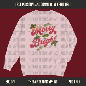 May include: A light pink sweatshirt with the words "Merry and Bright" in red script, accented with green holly and sprigs. The text is in a vintage style. The sweatshirt is a long-sleeved crew neck.