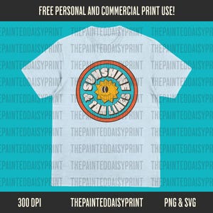 May include: A light blue t-shirt with a circular graphic design. The graphic features a yellow sun with a smiling face, surrounded by a blue circle with the text "Sunshine & Jam Lines" in orange and white.
