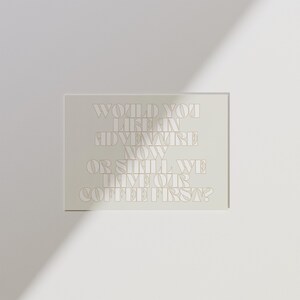 Peut inclure: Impression rectangulaire avec le texte "WOULD YOU LIKE AN ADVENTURE NOW OR SHALL WE HAVE OUR COFFEE FIRST ?" en beige clair. L'impression est posée sur un fond blanc avec une ombre.