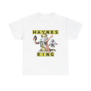 May include: White t-shirt with a graphic of a football player in a gold helmet and jersey, with the name "HAYNES KING" in yellow block letters. The player is throwing a football. The shirt is made of a soft, comfortable material.