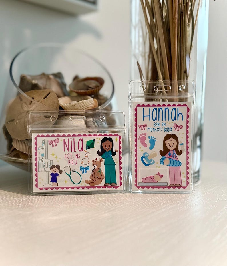 May include: Two clear plastic name badge holders with colorful illustrations. One says "Nila" with medical-themed graphics, and the other says "Hannah" with baby-related images. Both have pink borders and are on a white surface.