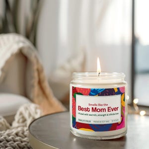 以下が含まれることがあります： カラフルなラベルが付いた白いキャンドル。ラベルには「Smells like the Best Mom Ever」と「Infused with warmth, strength & infinite love」の文字が書かれています。ラベルには「CAMILLE'S FIELDS - PREMIUM SOY WAX - 50 HOURS」の文字も書かれています。