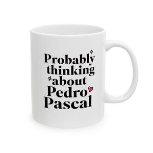 Puede incluir: Taza de cer&aacute;mica blanca con la frase "Probably thinking about Pedro Pascal" en negro. La taza tiene un asa curva y un peque&ntilde;o coraz&oacute;n rojo. Un regalo divertido.