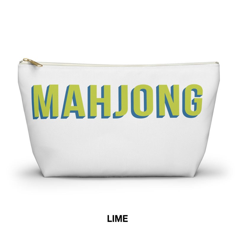 May include: A white zippered pouch featuring the word MAHJONG printed in large, lime green block letters with a blue shadow effect. The pouch has a gold-toned metal zipper pull at the top left corner and a simple, tapered rectangular shape.
