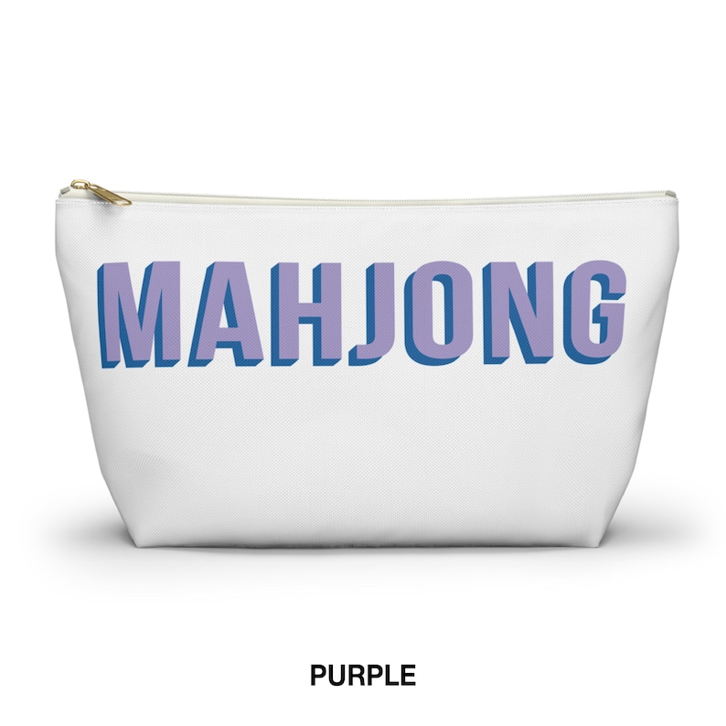 May include: A white zippered pouch featuring the word MAHJONG printed in large, block-style letters. The text has a light purple face with a dark blue shadow effect, creating a three-dimensional appearance against the plain white background.