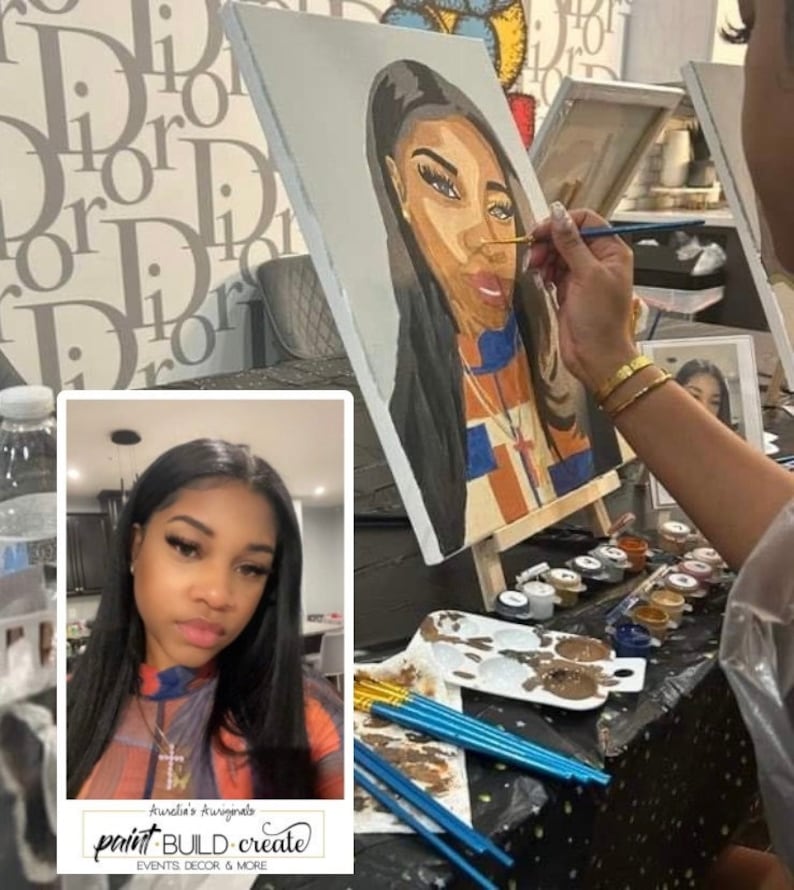 May include: A woman paints a portrait of another woman on a canvas. The portrait is in progress and the woman painting is using a brush to add details to the face. The woman in the portrait has dark hair and is wearing a colorful shirt. The woman painting is wearing a white shirt and a gold bracelet. The image also includes a photo booth with a woman in it. The photo booth has a sign that says "Auntie's Awakenings paint BUILD create EVENTS DECOR & MORE".