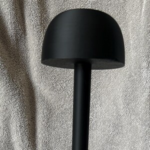 May include: A black mannequin head stand with a round head and a tall, cylindrical base. The base has a starburst design with five points.