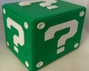 Op de afbeelding: Een groene doos met een wit vraagteken aan elke kant. De doos is gemaakt van plastic en heeft een scharnierend deksel.