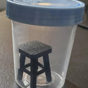 Può includere: Un contenitore di plastica trasparente con un coperchio blu. Il contenitore ha uno sgabello nero piccolo all'interno. Il contenitore ha il testo "TOOT" e "ROOM" stampato sul lato.