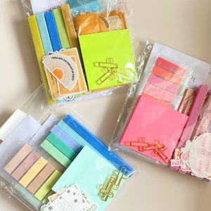 Puede incluir: Varios juegos de papelería en bolsas de plástico transparente. Cada juego incluye notas adhesivas, resaltadores, clips y pegatinas. Las pegatinas tienen el texto "I WILL GIVE YOU THE GIFT OF PEACE" y "EVEN IF FAITH".